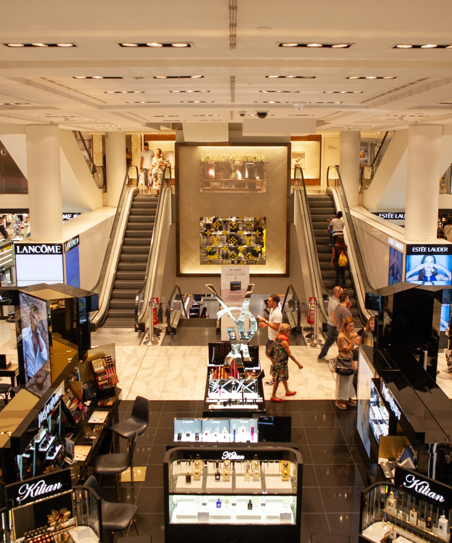 Interior of a shopping mall with escalators and cosmetic displays showcasing retail lighting.