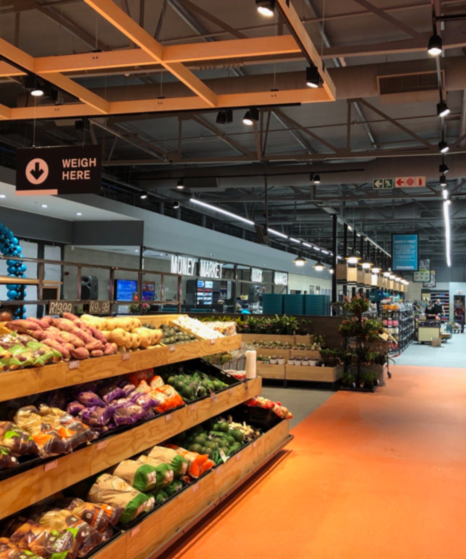 Interior of a grocery store lighting with produce section and signs on the ceiling.